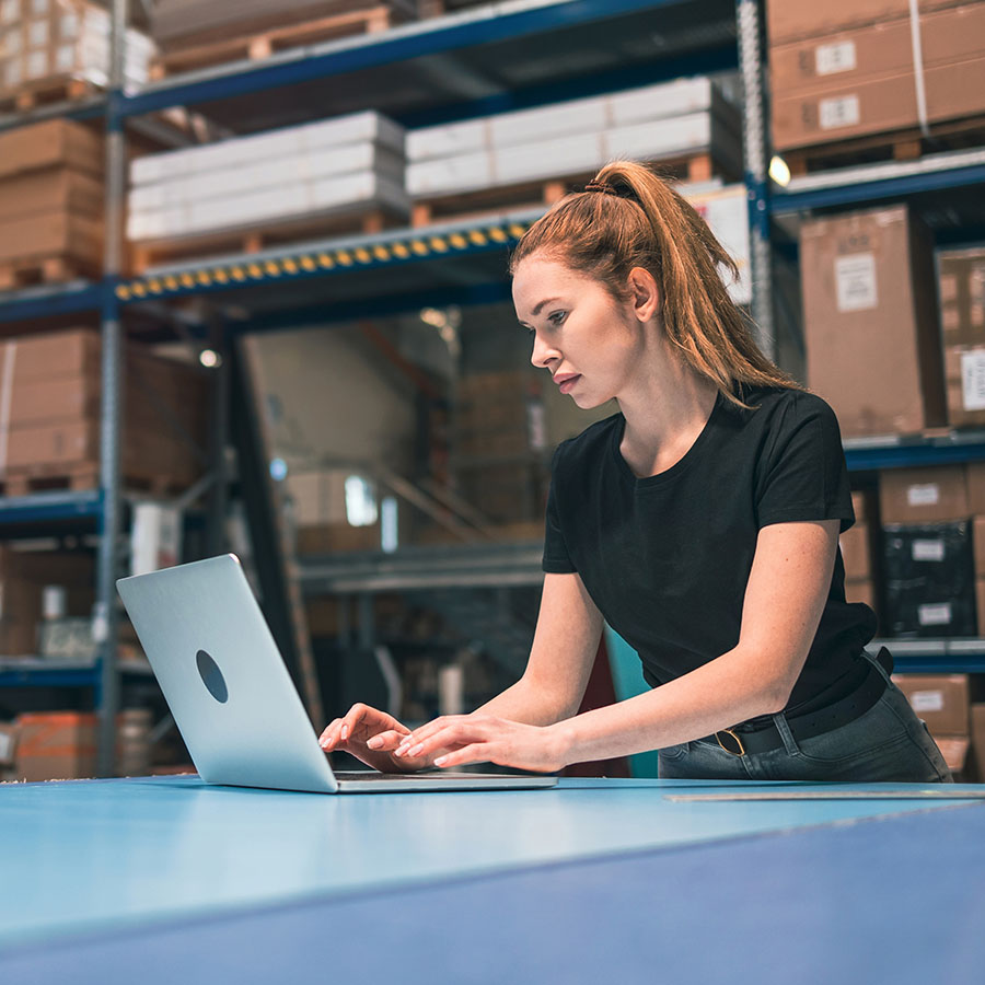 A woman in a warehouse managing inventory using a laptop, representing efficient stock handling for Yankee